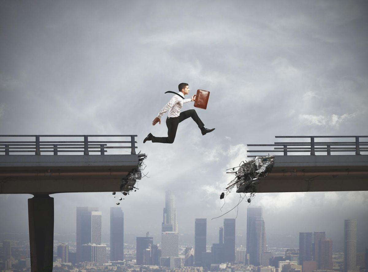 Businessman jumps over missing piece of a broken bridge