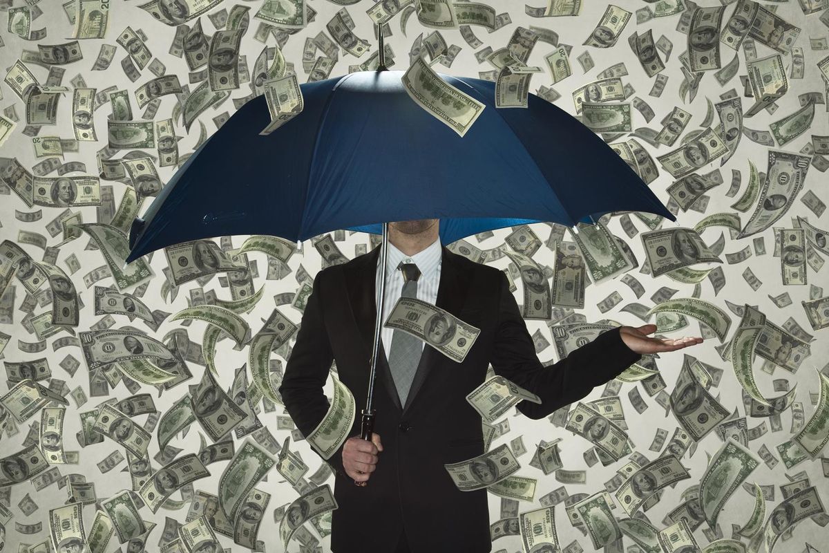 Businessman under umbrella in dollar bill rain