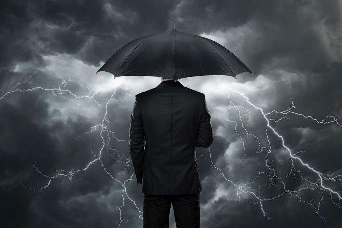 Businessman with umbrella standing in front of storm