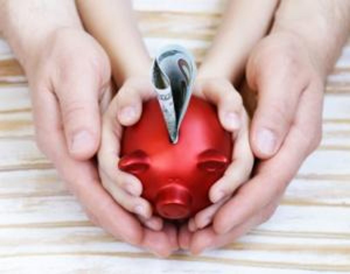 close up of father and son hands holding red piggy bank