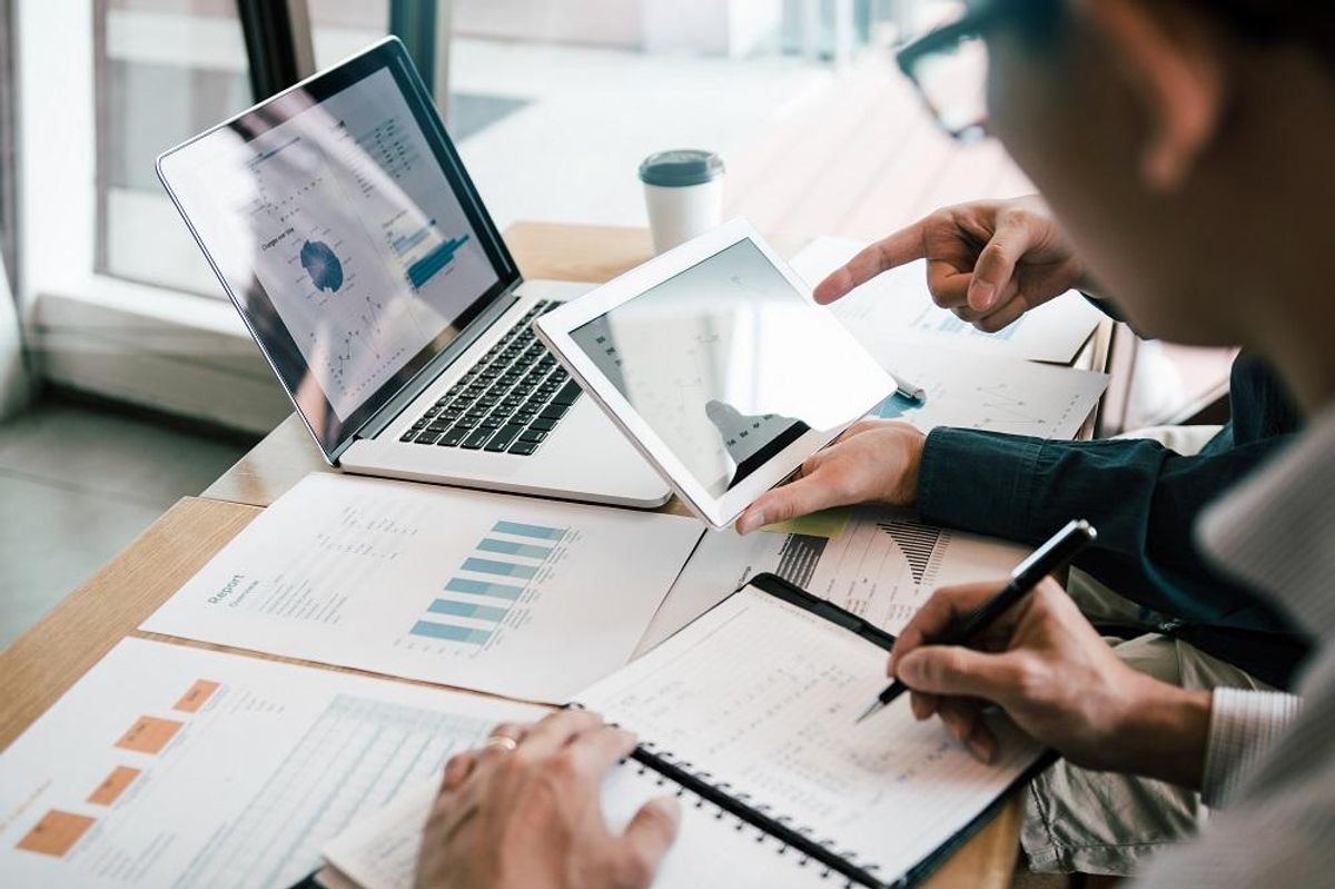 Coworkers use a tablet and laptop to do competitor analysis