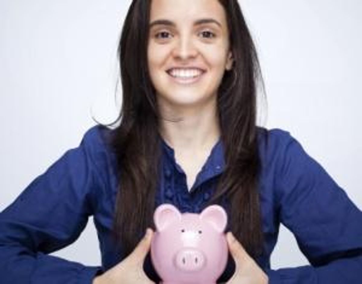 Happy smiling woman holding a piggy bank against gray background