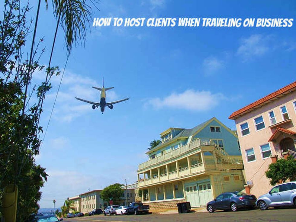 How to Host Clients When Traveling On Business: Photo of airplane in blue sky landing near multi-story buildings -- business trip