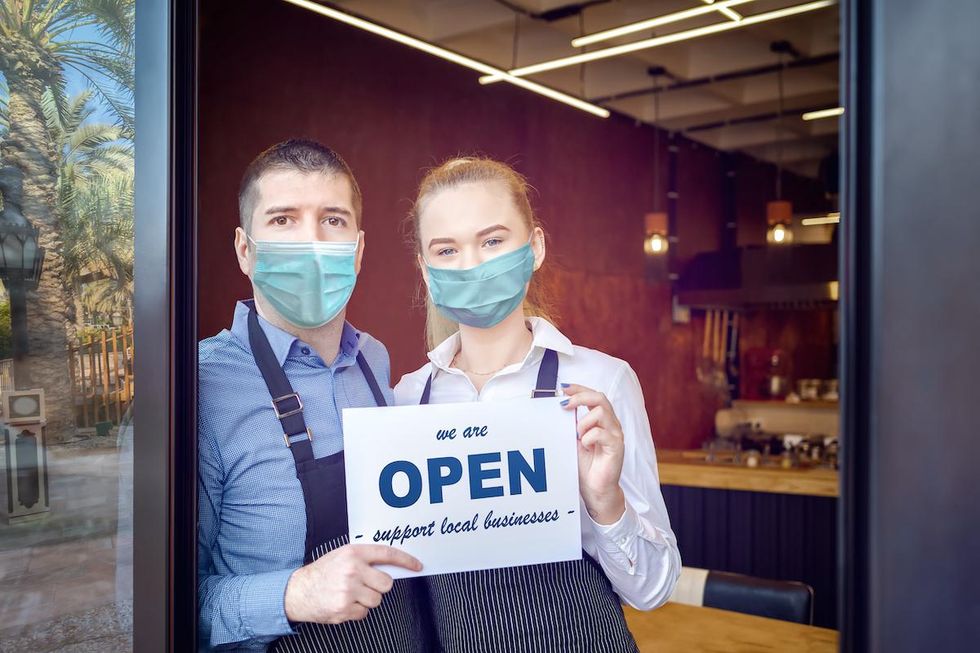 small business owners in face masks holding open sign