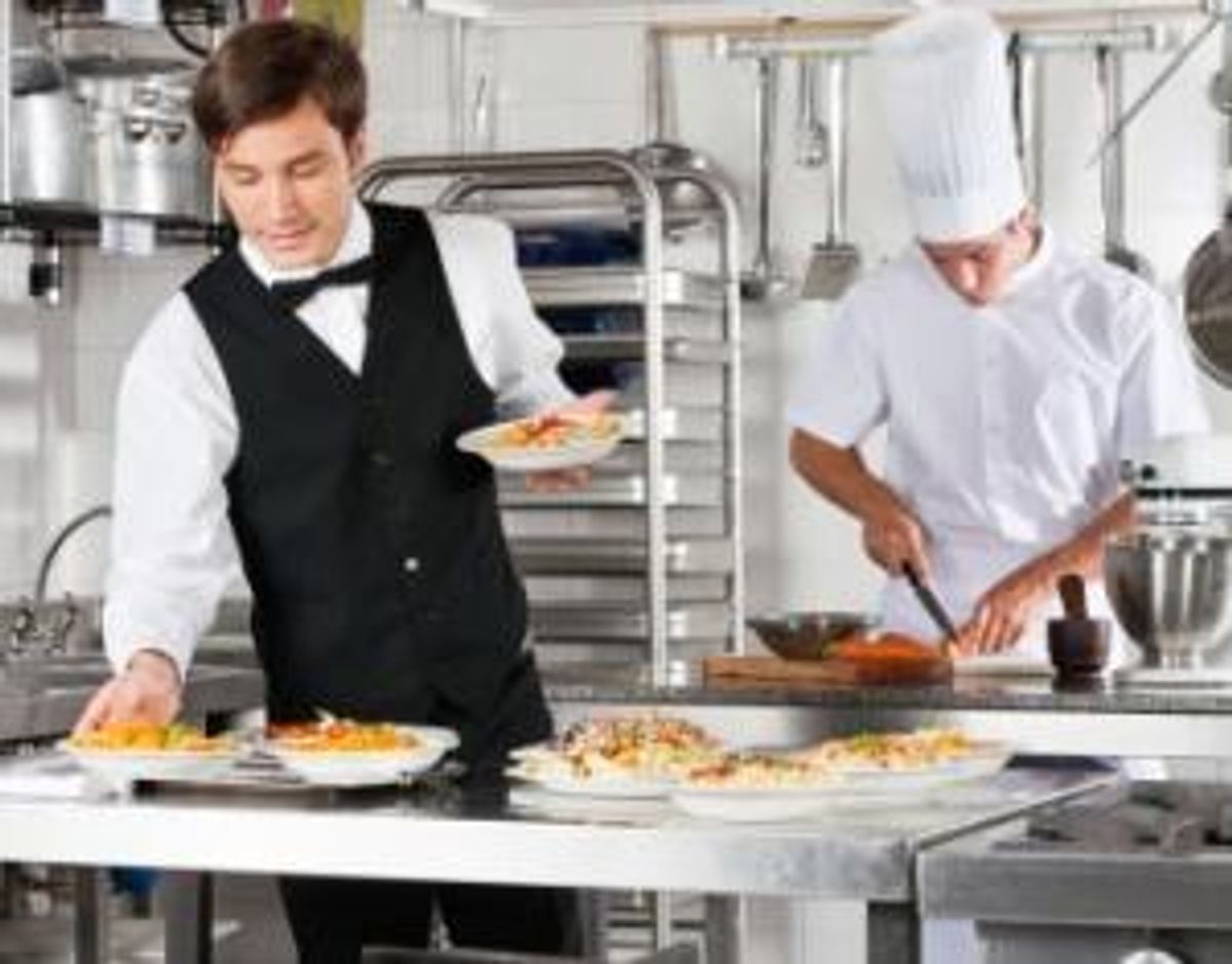 Waiter And Chef Working In Commercial Kitchen