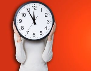 Woman holding a clock over face against orange background. Time concept