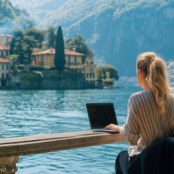 Young woman working remotely by a scenic lake in Italy, calm and focused